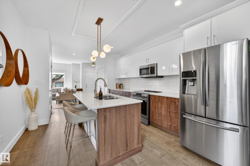 The kitchen features a large island with seating, a stainless steel refrigerator, white upper cabinetry, and wood-toned lower cabinetry - 7624 91 Avenue, Edmonton, AB - Indoor Photo Showing Kitchen With Stainless Steel Kitchen With Upgraded Kitchen