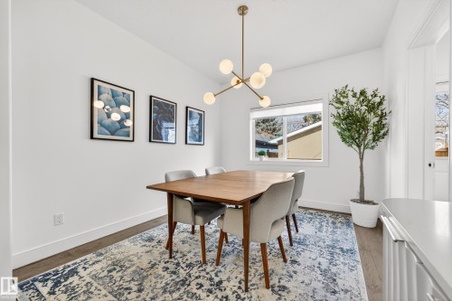 The dining area features a modern chandelier, a window providing natural light, hardwood floors, and a blue and white patterned area rug - 7624 91 Avenue, Edmonton, AB - Indoor Photo Showing Dining Room