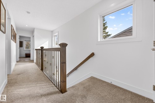 The property features a staircase with a dark wood railing and metal spindles, complemented by light-colored carpeting - 7624 91 Avenue, Edmonton, AB - Indoor Photo Showing Other Room