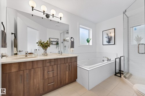 Bathroom featuring a double vanity with ample storage, a large mirror with contemporary lighting, a built-in bathtub, and a glass-enclosed shower - 7624 91 Avenue, Edmonton, AB - Indoor Photo Showing Bathroom