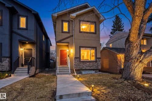 The property features a stucco exterior with stone accents, a red front door, and illuminated windows - 7624 91 Avenue, Edmonton, AB - Outdoor