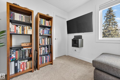 This room features carpeted flooring, a window offering views of mature trees, and a wall-mounted television - 7624 91 Avenue, Edmonton, AB - Indoor