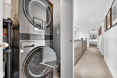 This property features a stacked washer and dryer unit, and a hallway with light-colored carpeting, white walls, recessed lighting, and framed artwork - 7624 91 Avenue, Edmonton, AB - Indoor Photo Showing Laundry Room