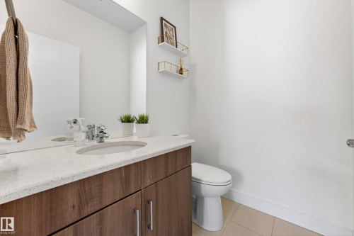 The bathroom features a vanity with a white countertop and a built-in sink, a large mirror, and a toilet - 7624 91 Avenue, Edmonton, AB - Indoor Photo Showing Bathroom