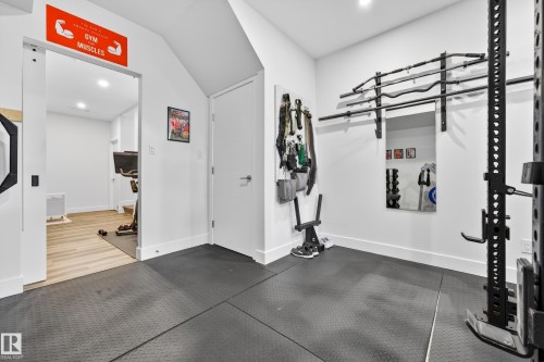 Dedicated fitness area featuring rubber mat flooring, wall-mounted racks for equipment, and a functional mirror - 7624 91 Avenue, Edmonton, AB - Indoor Photo Showing Gym Room