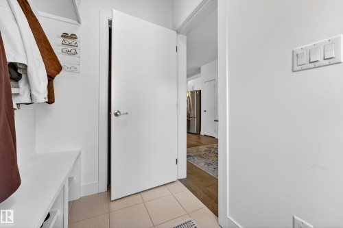 Entryway featuring light-toned floor tiles, a white built-in bench, and a modern white door with a silver handle - 7624 91 Avenue, Edmonton, AB - Indoor