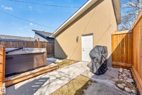 The property features a private outdoor area with a hot tub on a wooden deck, a paved walkway, and a fenced perimeter - 7624 91 Avenue, Edmonton, AB - Outdoor With Exterior