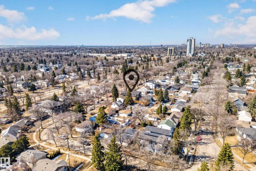 Aerial view of the surrounding neighborhood, featuring residential properties, mature trees, and a distant cityscape under a blue sky with clouds - 7624 91 Avenue, Edmonton, AB - Outdoor With View