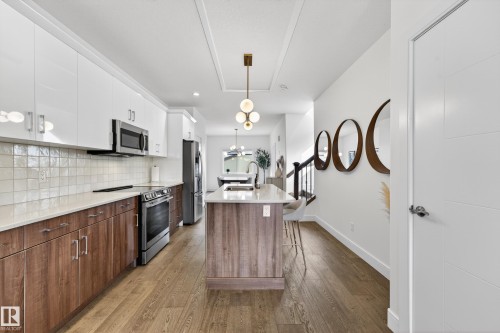 The kitchen features hardwood floors, a central island with a countertop, stainless steel appliances, and white upper cabinetry - 7624 91 Avenue, Edmonton, AB - Indoor Photo Showing Kitchen With Upgraded Kitchen