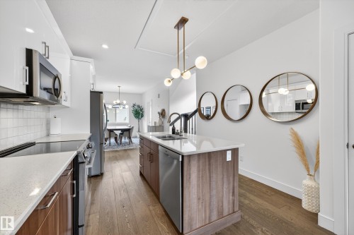 The kitchen features white upper cabinetry, natural wood lower cabinetry, and stainless steel appliances, including a microwave, oven, and dishwasher - 7624 91 Avenue, Edmonton, AB - Indoor Photo Showing Kitchen With Double Sink With Upgraded Kitchen