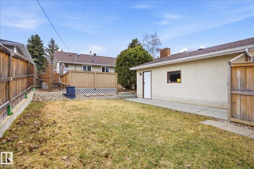 Spacious backyard featuring a manicured lawn, concrete walkway, detached structure with a side entrance, wooden privacy fence, and an elevated wood deck - 10222 73 Street, Edmonton, AB 