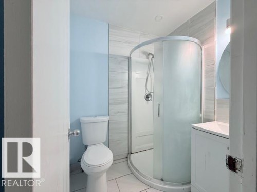 Bathroom featuring a curved glass shower enclosure, a toilet, a vanity with a sink, and light-colored wall tiles - 2831 36 Street, Edmonton, AB - Indoor Photo Showing Bathroom