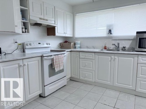 The kitchen features white cabinetry, stone countertops, a white electric range, and a window with blinds - 2831 36 Street, Edmonton, AB - Indoor Photo Showing Kitchen