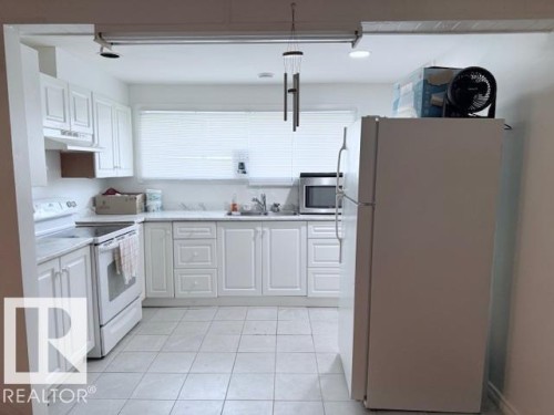 The kitchen features white cabinetry, white appliances, and tiled flooring - 2831 36 Street, Edmonton, AB - Indoor Photo Showing Kitchen With Double Sink