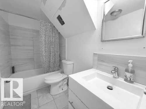 Bathroom featuring a bathtub with tiled surround, a toilet, and a vanity with a sink and faucet - 2831 36 Street, Edmonton, AB - Indoor Photo Showing Bathroom