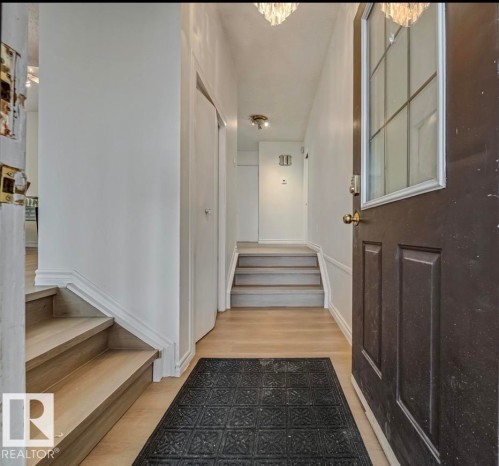 Welcoming entryway with a dark paneled door, light-toned flooring, and a staircase featuring light wooden treads and white risers - 2831 36 Street, Edmonton, AB - Indoor Photo Showing Other Room
