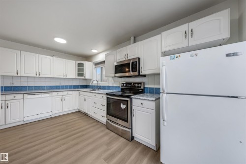 Kitchen featuring white cabinetry, a blue tiled backsplash, stainless steel appliances, and light wood-look flooring - 2831 36 Street, Edmonton, AB - Indoor Photo Showing Kitchen