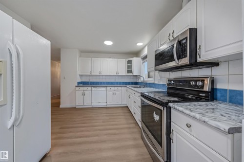 The kitchen features white cabinetry, a blue and white tiled backsplash, and stainless steel appliances including a microwave and range - 2831 36 Street, Edmonton, AB - Indoor Photo Showing Kitchen