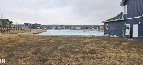 The property features a large yard with views of a body of water and other residential structures in the distance - 13 Sunset Harbour, Rural Wetaskiwin County, AB 
