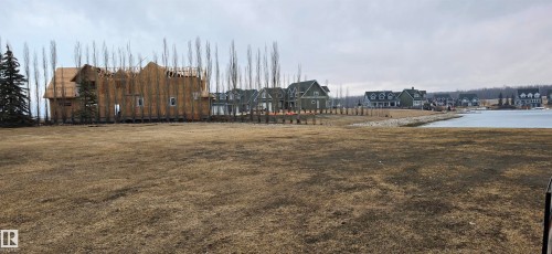 The property features a large grassy area, a visible body of water, and surrounding properties with varying architectural styles - 13 Sunset Harbour, Rural Wetaskiwin County, AB 