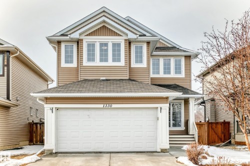 The property features light brown siding, white trim, and a prominent attached garage with a white door - 1330 114B Street, Edmonton, AB - Outdoor With Facade