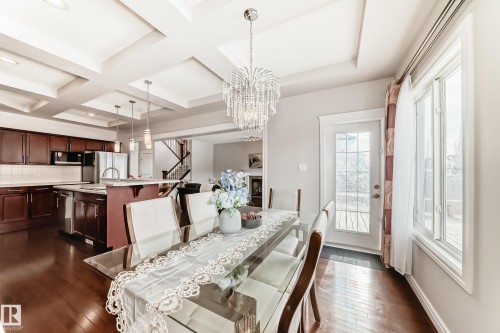 The property features an open-concept living space with dark wood flooring, a kitchen with dark cabinetry and stainless steel appliances, and a dining area illuminated by a large crystal chandelier - 1330 114B Street, Edmonton, AB - Indoor Photo Showing Dining Room