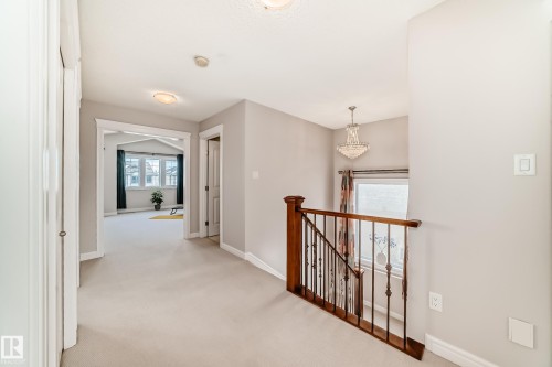Bright hallway with light-colored carpeting, a wooden and metal staircase railing, and a decorative chandelier illuminating the stairwell - 1330 114B Street, Edmonton, AB - Indoor Photo Showing Other Room