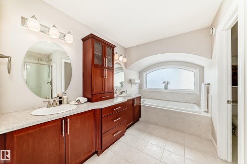 Bathroom featuring a double vanity with wooden cabinetry, an arched window above a built-in bathtub, and tiled flooring - 1330 114B Street, Edmonton, AB - Indoor Photo Showing Bathroom