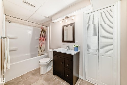 Bathroom featuring tiled flooring, a shower-tub combination, a vanity with a white sink, and white louvered bifold doors - 1330 114B Street, Edmonton, AB - Indoor Photo Showing Bathroom