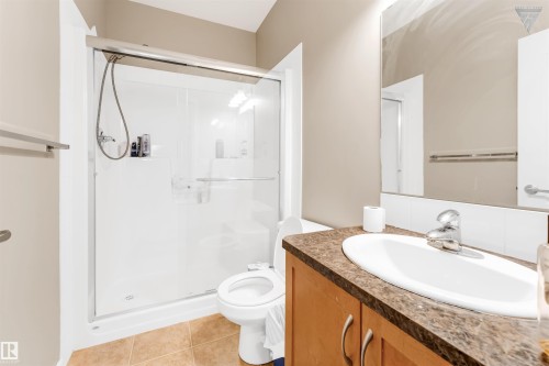 The bathroom features a shower with a sliding glass door, a toilet, a vanity with a white sink and a chrome faucet, and a large mirror - #418 392 Silver Berry Road Nw, Edmonton, AB - Indoor Photo Showing Bathroom