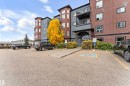Exterior view of the property showcasing the main entrance with an arched stone entryway, balconies, and an adjacent paved parking area - #418 392 Silver Berry Road Nw, Edmonton, AB  - Outdoor With Balcony With Facade 