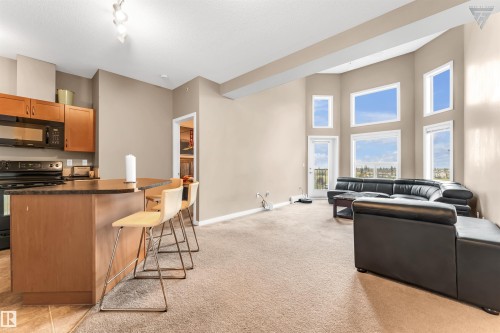 The property features a kitchen with wood cabinetry and black appliances, including a microwave and range - #418 392 Silver Berry Road Nw, Edmonton, AB - Indoor