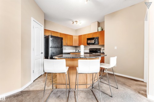 The kitchen features wooden cabinetry, black appliances, and a central island with a granite-style countertop - #418 392 Silver Berry Road Nw, Edmonton, AB - Indoor Photo Showing Kitchen