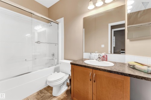 The bathroom features a vanity with a laminate countertop and a drop-in sink, a large mirror, and a bathtub with a shower and sliding glass doors - #418 392 Silver Berry Road Nw, Edmonton, AB - Indoor Photo Showing Bathroom