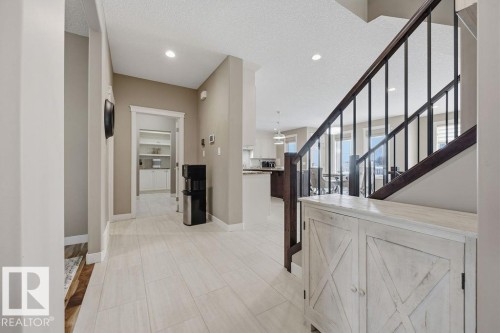 The entryway features light-toned tiled flooring, a staircase with dark wood handrails and black balusters, and recessed ceiling lighting - 76 Newgate Way, St. Albert, AB - Indoor Photo Showing Other Room