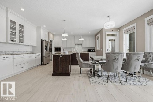 This kitchen and dining area features light-toned flooring, white cabinetry with glass-front accents, and a dark-toned kitchen island with a light-toned countertop - 76 Newgate Way, St. Albert, AB - Indoor