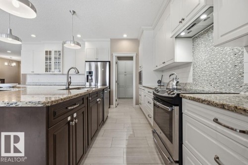 The kitchen features a large island with a granite countertop and a stainless steel sink, white upper cabinetry, and dark lower cabinetry - 76 Newgate Way, St. Albert, AB - Indoor Photo Showing Kitchen With Upgraded Kitchen