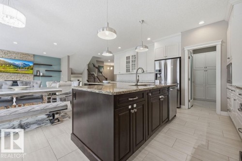 The kitchen features a large island with granite countertops, a stainless steel refrigerator, and ample cabinetry - 76 Newgate Way, St. Albert, AB - Indoor Photo Showing Kitchen With Upgraded Kitchen
