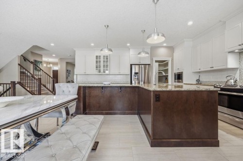 The kitchen features white upper cabinetry, a dark wood island with light-colored countertops, stainless steel appliances, and pendant lighting - 76 Newgate Way, St. Albert, AB - Indoor Photo Showing Kitchen With Upgraded Kitchen