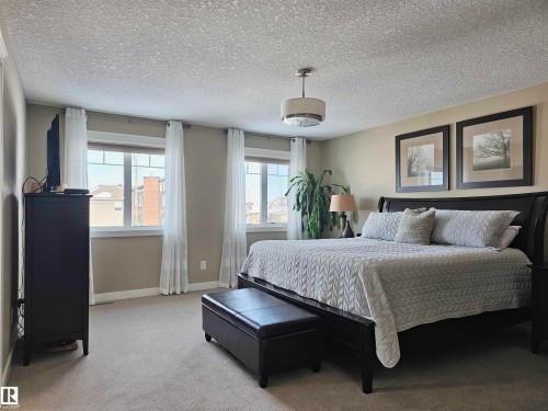 This room features light-colored carpeting, two windows with white curtains, and a ceiling light fixture - 76 Newgate Way, St. Albert, AB - Indoor Photo Showing Bedroom