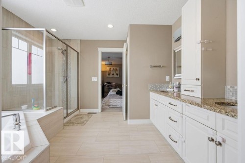 Bathroom featuring a glass-enclosed shower, a large bathtub, light tile flooring, and a double vanity with granite countertops and white cabinetry - 76 Newgate Way, St. Albert, AB - Indoor