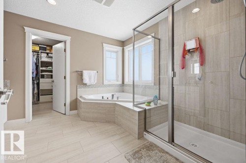 The bathroom features a corner bathtub, a glass-enclosed shower, and light-toned tile flooring - 76 Newgate Way, St. Albert, AB - Indoor Photo Showing Bathroom