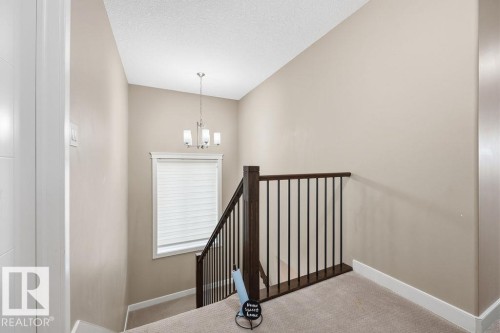 The property features a staircase with dark wood railings and black spindles, leading to a landing with light-colored carpeting - 76 Newgate Way, St. Albert, AB - Indoor Photo Showing Other Room