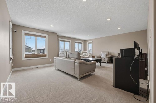 This spacious living area features neutral-toned carpeting and walls, recessed lighting, and multiple windows with blinds - 76 Newgate Way, St. Albert, AB - Indoor
