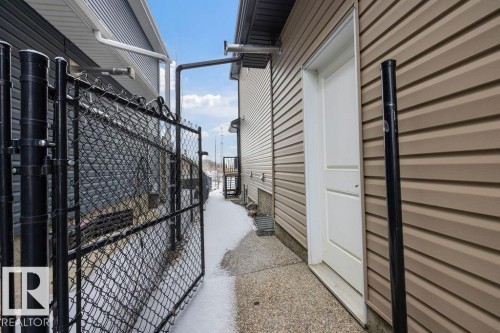 The property features tan siding, a white exterior door, and a black chain link fence - 76 Newgate Way, St. Albert, AB - Outdoor With Exterior