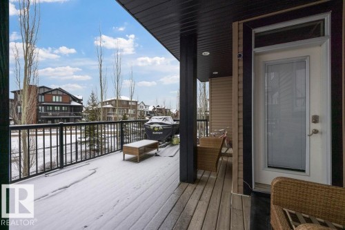 This property features a spacious deck with wood flooring and a black metal railing, offering views of surrounding homes and bare trees under a blue sky - 76 Newgate Way, St. Albert, AB - Outdoor With Deck Patio Veranda With Exterior