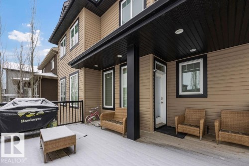 The property features an outdoor deck area with a covered patio, tan siding, and black trim - 76 Newgate Way, St. Albert, AB - Outdoor With Deck Patio Veranda With Exterior