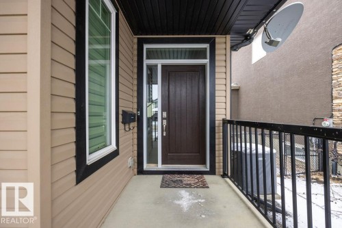 The property features a front entrance with a dark wood door, a side window, and beige siding - 76 Newgate Way, St. Albert, AB - Outdoor With Exterior