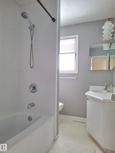 Bathroom with white bathtub and shower fixture, a single vanity with a mirror, and a window providing natural light - 13112 63 Avenue, Edmonton, AB - Indoor Photo Showing Bathroom