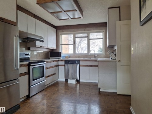 The kitchen features white cabinetry with wood trim, stainless steel appliances, and a window above the sink - 13112 63 Avenue, Edmonton, AB - Indoor Photo Showing Kitchen